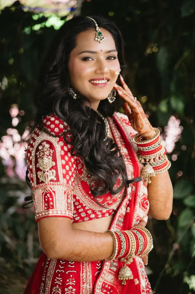 Smiling Indian bride in a red embroidered lehenga with traditional jewelry and bridal mehndi near Triyuginarayan Temple.