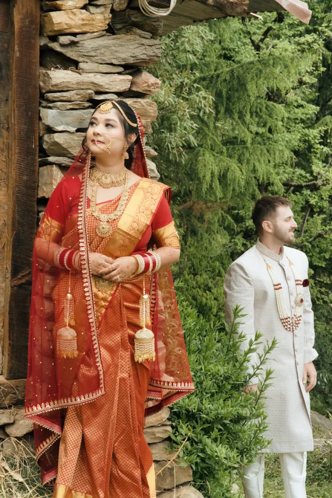 Bride and groom posing beside a traditional stone house surrounded by greenery
