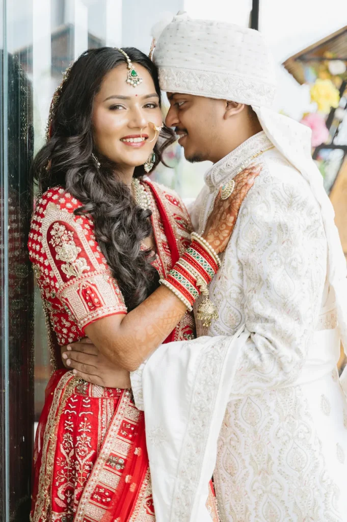 Close-up portrait of a smiling Indian bride in a red lehenga and groom in a white sherwani embracing during their wedding near Triyuginarayan Temple.