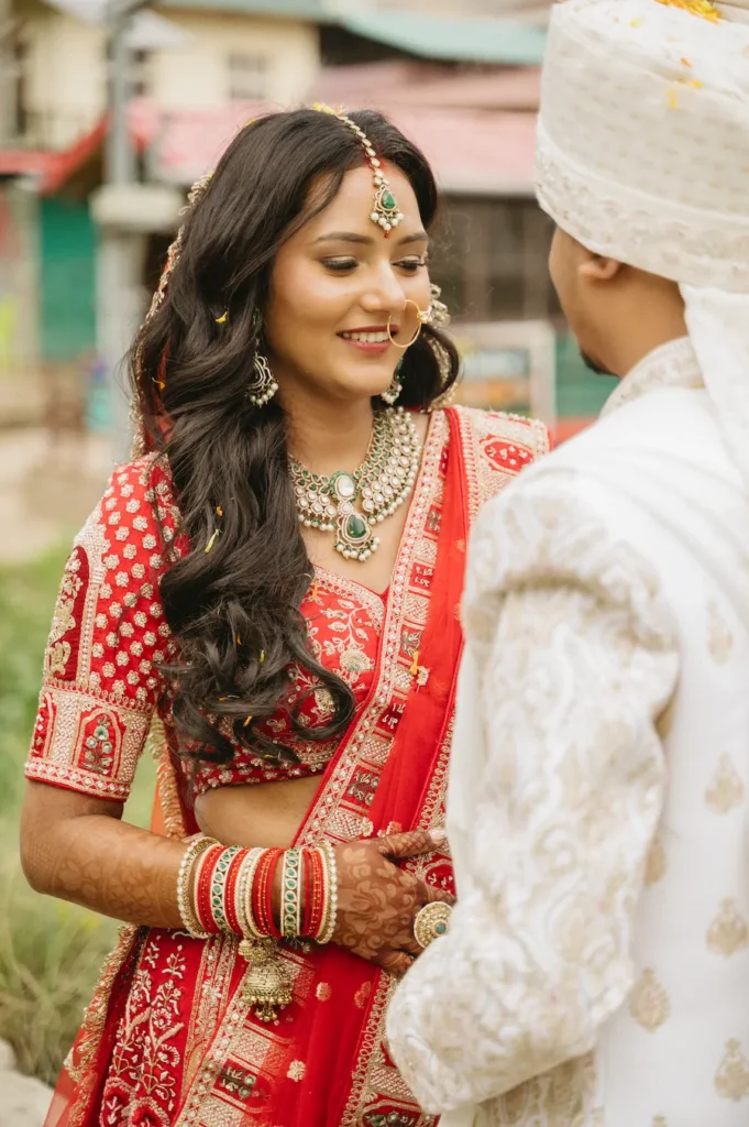 Close-up candid portrait of a smiling Indian bride in a red lehenga standing next to her groom in a white sherwani near Triyuginarayan Temple.