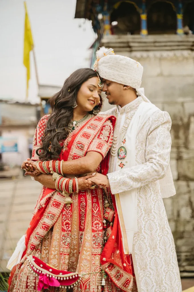 Indian bride and groom sharing a tender embrace, resting their foreheads together in traditional wedding attire outside Triyuginarayan Temple.