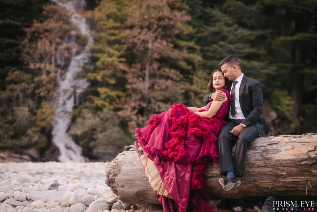 Creative pre-wedding photoshoot featuring a couple sharing a romantic moment beside a scenic riverside waterfall in the mountains.