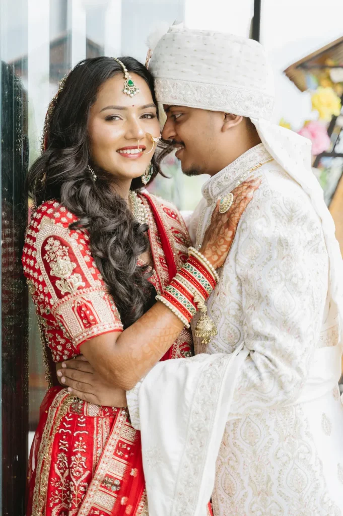 Close-up candid portrait of a smiling Indian bride in a red lehenga and groom in a white sherwani embracing during their wedding in Dehradun.