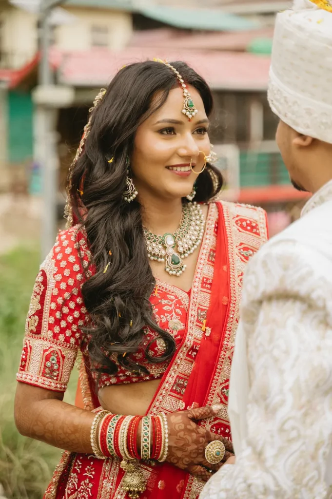 Close-up candid portrait of a smiling Indian bride in a red lehenga standing next to her groom in a white sherwani in Dehradun.