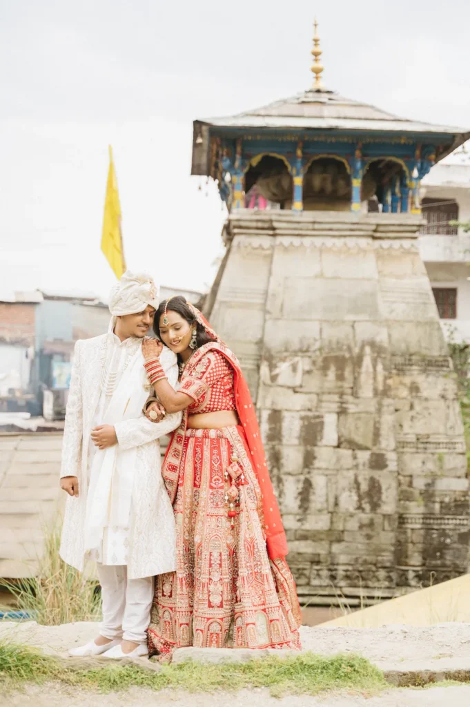 Indian newlywed couple embracing with the bride resting her head on the groom's shoulder by Triyuginarayan Temple.