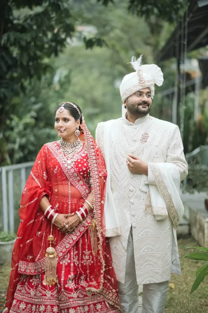 Bride and groom in traditional wedding attire posing together amid lush greenery.