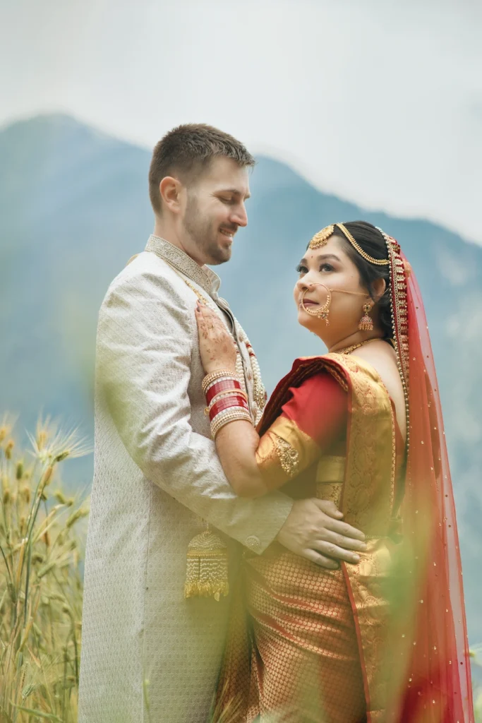 Bride and groom in traditional Indian wedding attire hugging in a mountain field near Triyuginarayan Temple.