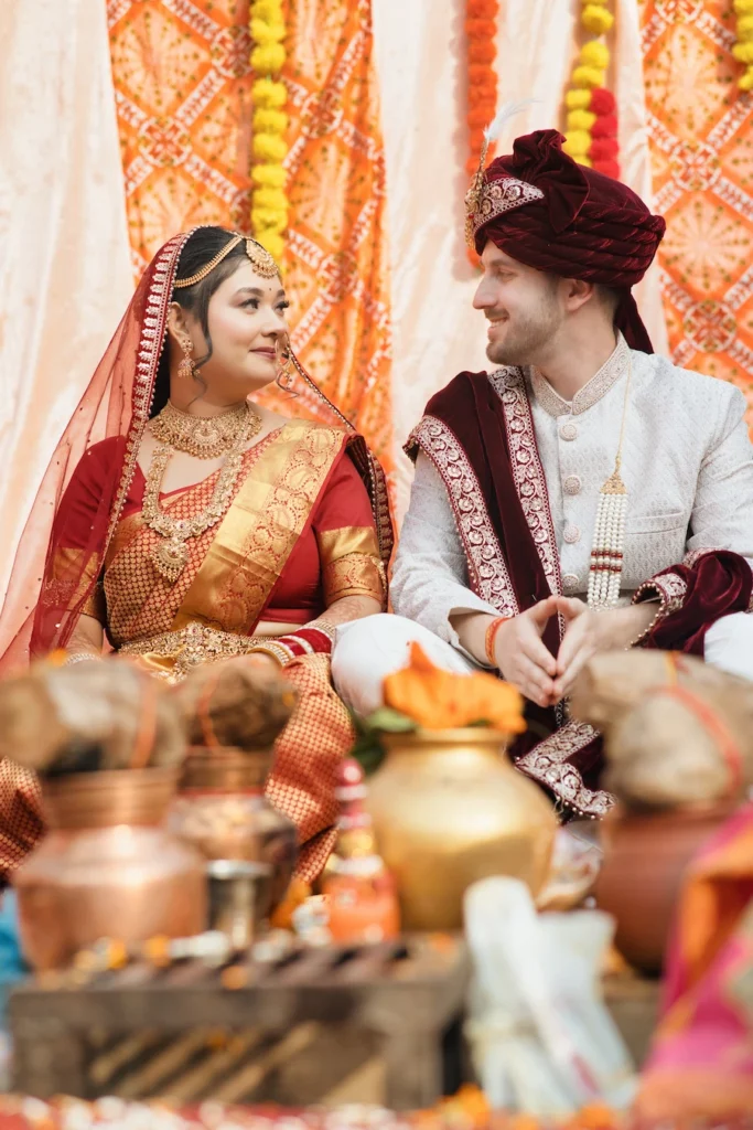 Bride and groom smiling at each other behind sacred Havan ritual pots during their wedding at Triyuginarayan Temple.