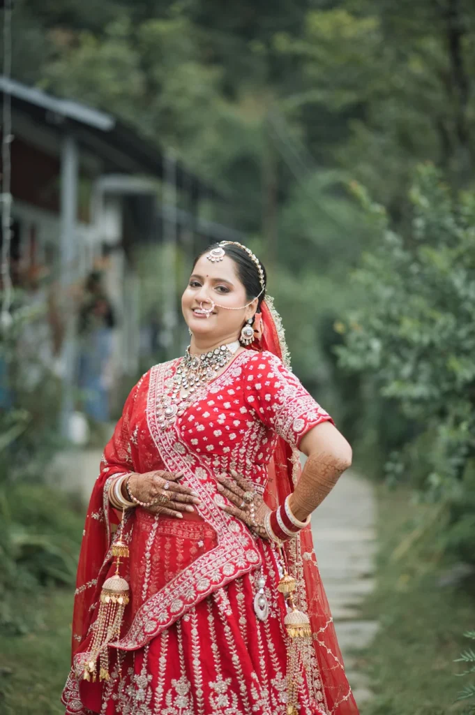 Bride in a traditional red lehenga posing gracefully on a quiet green pathway.