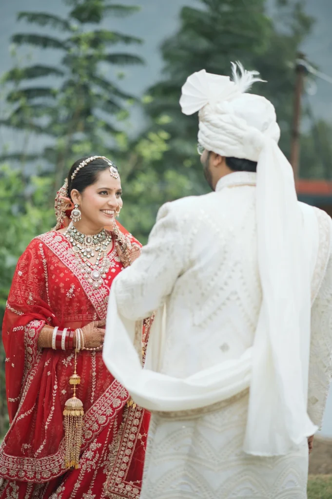 Bride and groom sharing a joyful wedding moment in traditional attire surrounded by greenery.