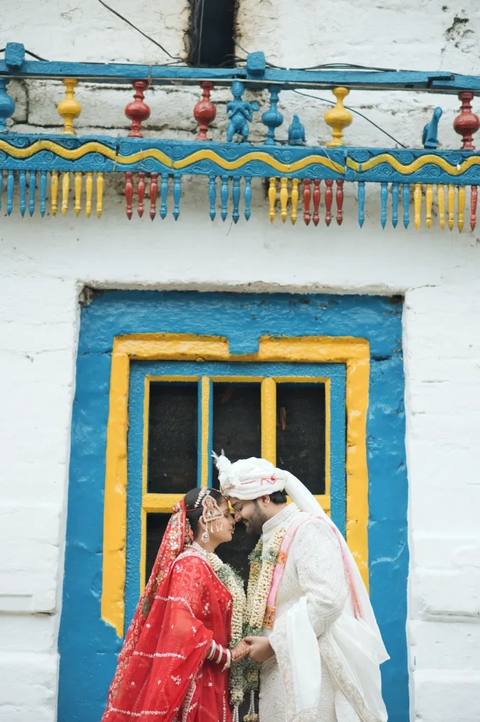 Bride and groom sharing an intimate wedding moment in front of a colorful traditional house.