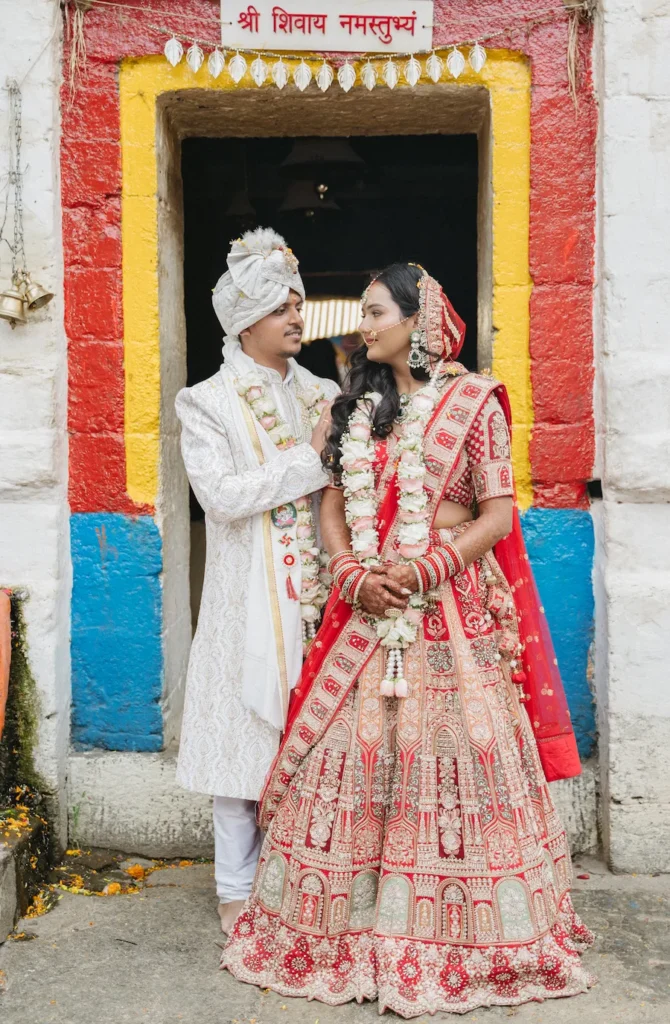 Indian bride and groom looking at each other standing in a brightly painted doorway at Triyuginarayan Temple.