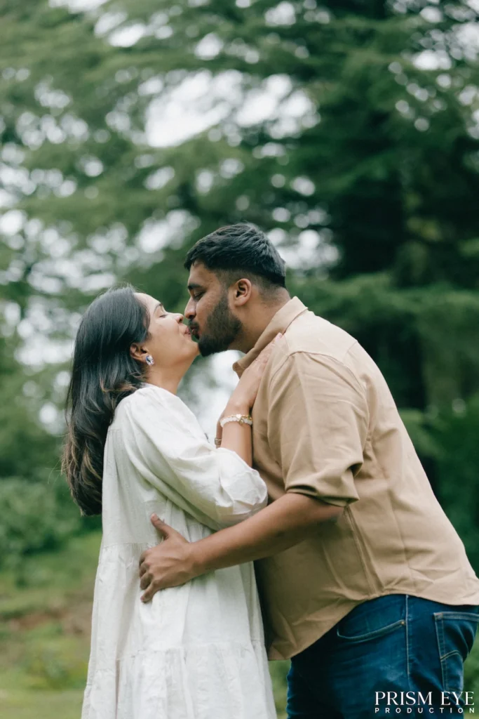 Couple sharing a candid kiss during a Monsoon Pre-Weddings shoot in Uttarakhand surrounded by lush green forest and misty hills.
