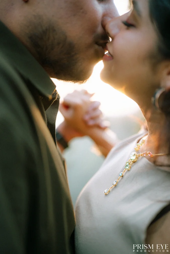 A couple sharing a soft kiss while holding hands in the evening light