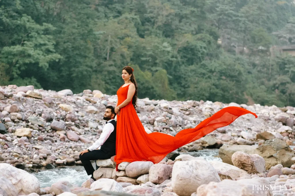 Couple posing in an orange flowing dress during a romantic pre-wedding photoshoot by the Ganga River in Rishikesh.