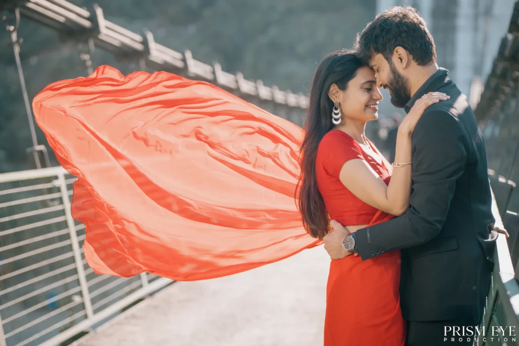 Couple sharing a romantic embrace during a proposal photoshoot by the Ganga in Rishikesh, with the bride's red dress flowing in the breeze.