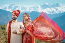 A cinematic wedding portrait where the bride's flowing dupatta adds elegance and movement against the breathtaking Himalayan landscape. Bride and groom with a flowing bridal dupatta against the Himalayan mountains during their destination wedding in Uttarakhand.