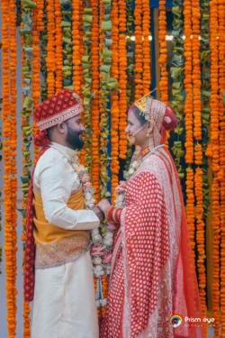 A heartwarming wedding portrait of the bride and groom sharing a joyful moment against a vibrant marigold floral backdrop. Bride and groom holding hands in front of a marigold floral backdrop during their traditional Hindu wedding ceremony.