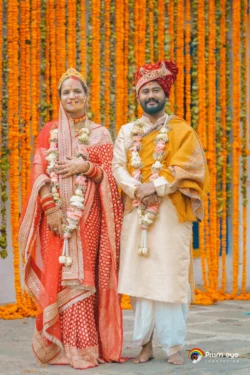 A joyful wedding portrait of the bride and groom standing together against a vibrant marigold floral backdrop, celebrating their special day. Bride and groom posing in traditional wedding attire before a vibrant marigold floral backdrop during their Hindu wedding ceremony.