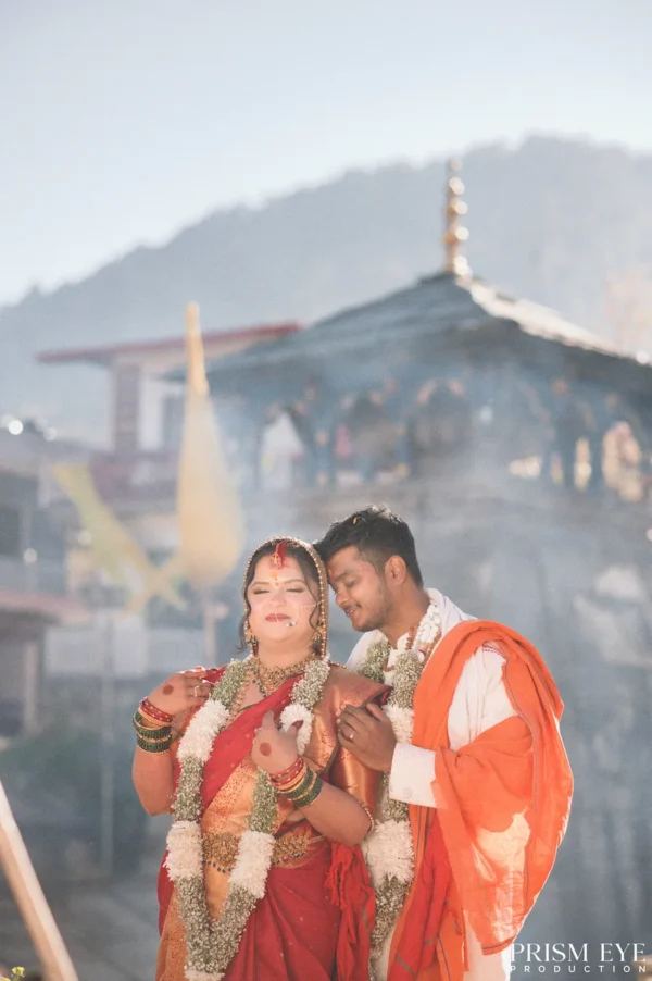 Couple celebrating with colorful Holi powder beneath a floral arch with Himalayan peaks in the background