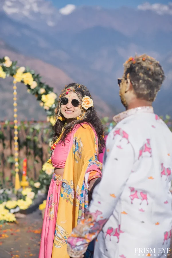 Couple holding hands beneath a floral arch with mountain views in the background