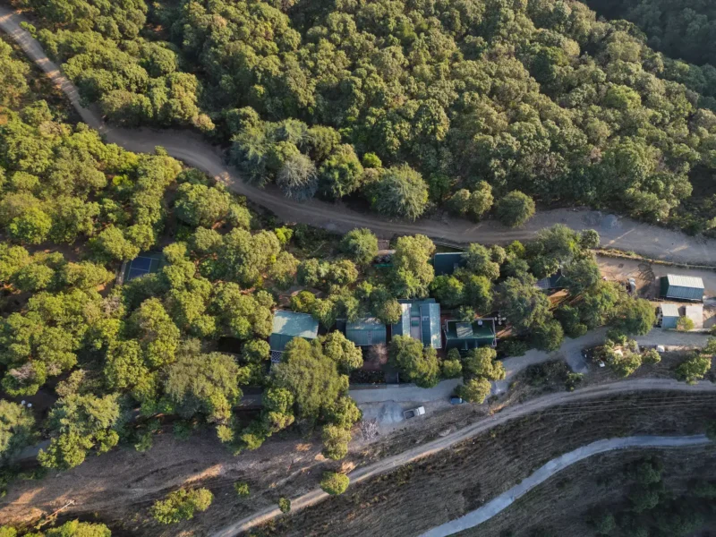 Scenic aerial view of a hillside villa and forest retreat in Dhanaulti with lush greenery and mountain surroundings. Aerial view of a hillside villa surrounded by dense forest in Dhanaulti, Uttarakhand.