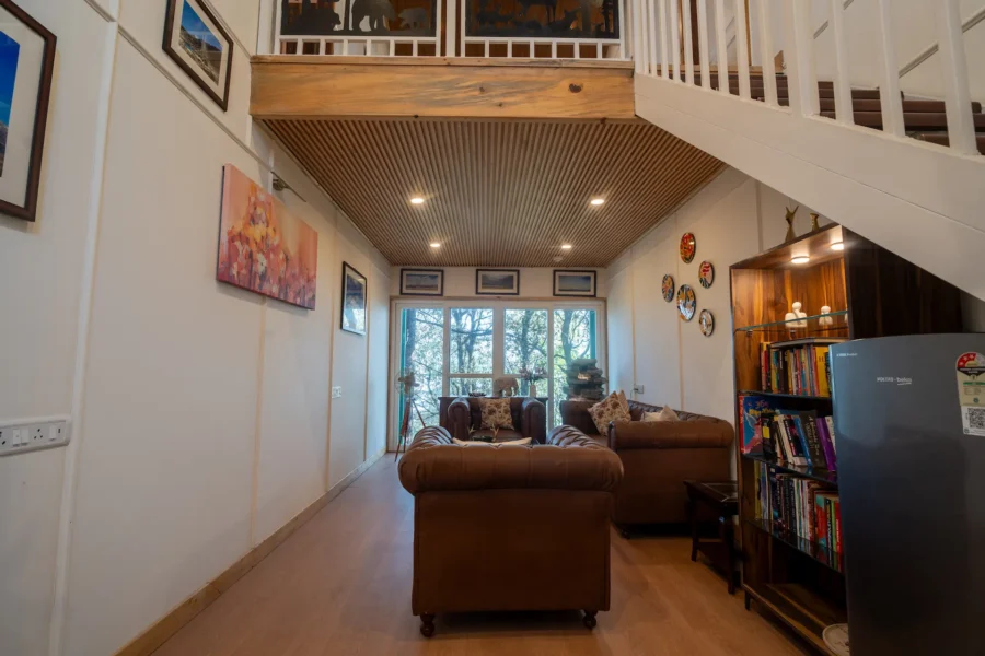 Elegant open-plan luxury villa living space in Mussoorie featuring a loft design, cozy seating, and scenic mountain-facing windows. Luxury villa living room with loft, wooden ceiling, and mountain view windows in Mussoorie, Uttarakhand.
