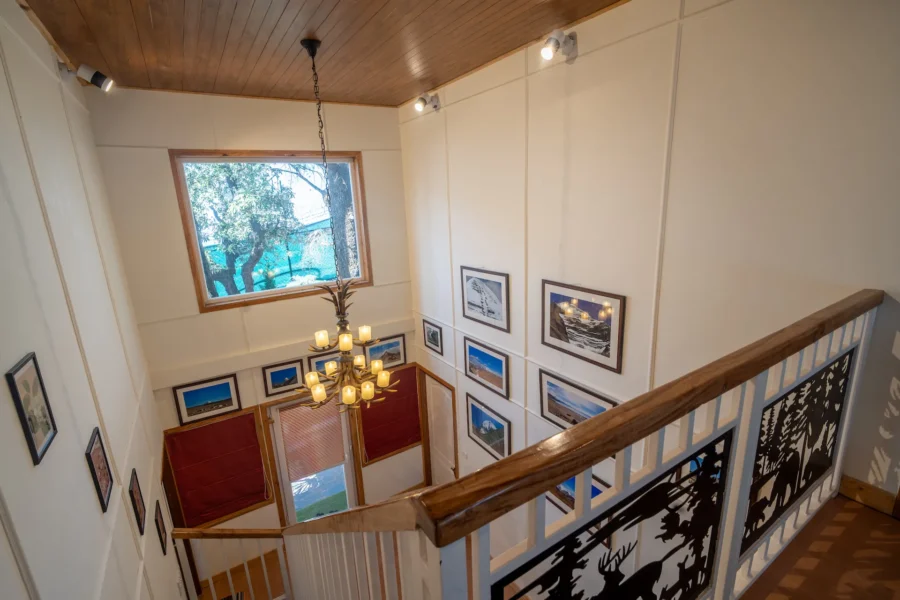 Beautiful villa staircase interior in Uttarakhand featuring wooden finishes, elegant lighting, and premium architectural design. Elegant wooden staircase interior with chandelier and framed artwork in a luxury villa in Uttarakhand.